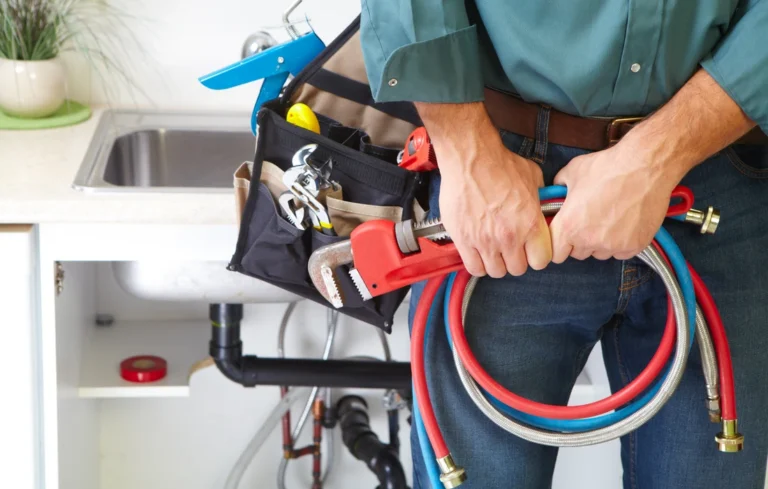 Plombier en tenue professionnelle tenant une clé à tuyau rouge, équipé d'une ceinture à outils noire contenant diverses clés