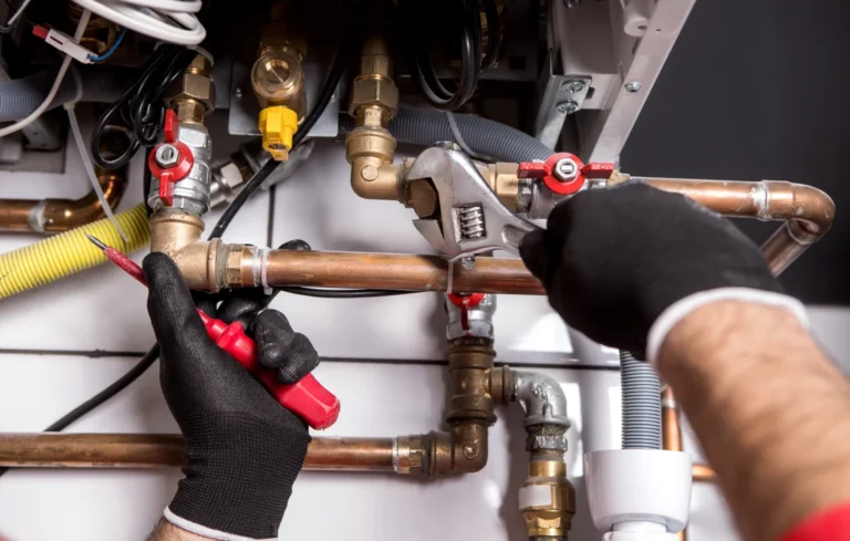 Plombier en gants noirs travaillant sur tuyauterie cuivre avec vannes rouges et outils de plomberie professionnels