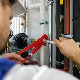 Plombier utilisant une clé à tuyauter rouge pour serrer une connexion de tuyauterie en PVC blanc sur une installation de